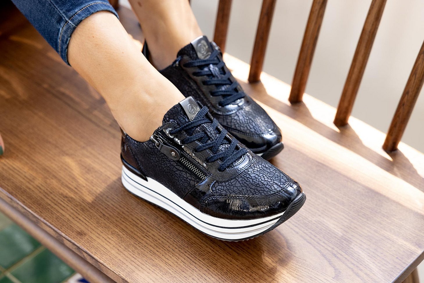Blaue Sneaker aus Kunstlack und Stretchmaterial mit Reißverschluss und Schnürung und Wechselfußbett. Passend zu den Schuhen trägt die Frau eine enge Jeanshose.