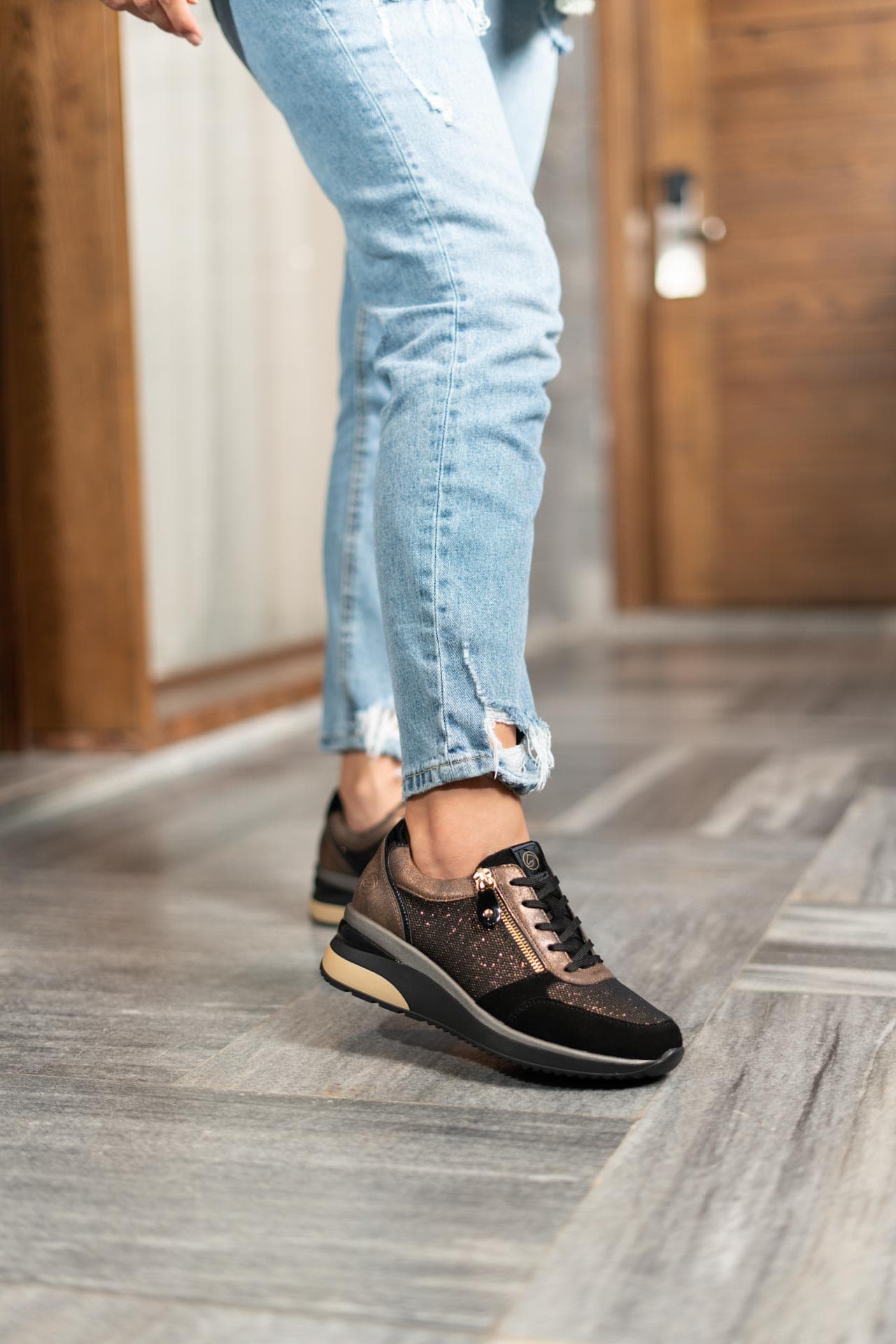 Schwarze Sneaker aus Veloursleder und Lederimitat mit Reißverschluss und Schnürung und Wechselfußbett. Passend zu den Schuhen trägt die Frau eine ripped Jeans.